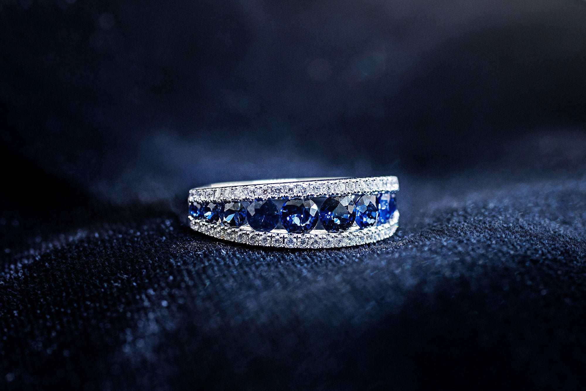 Graduated round blue sapphire band between two rows of pavé diamonds in 14K white gold